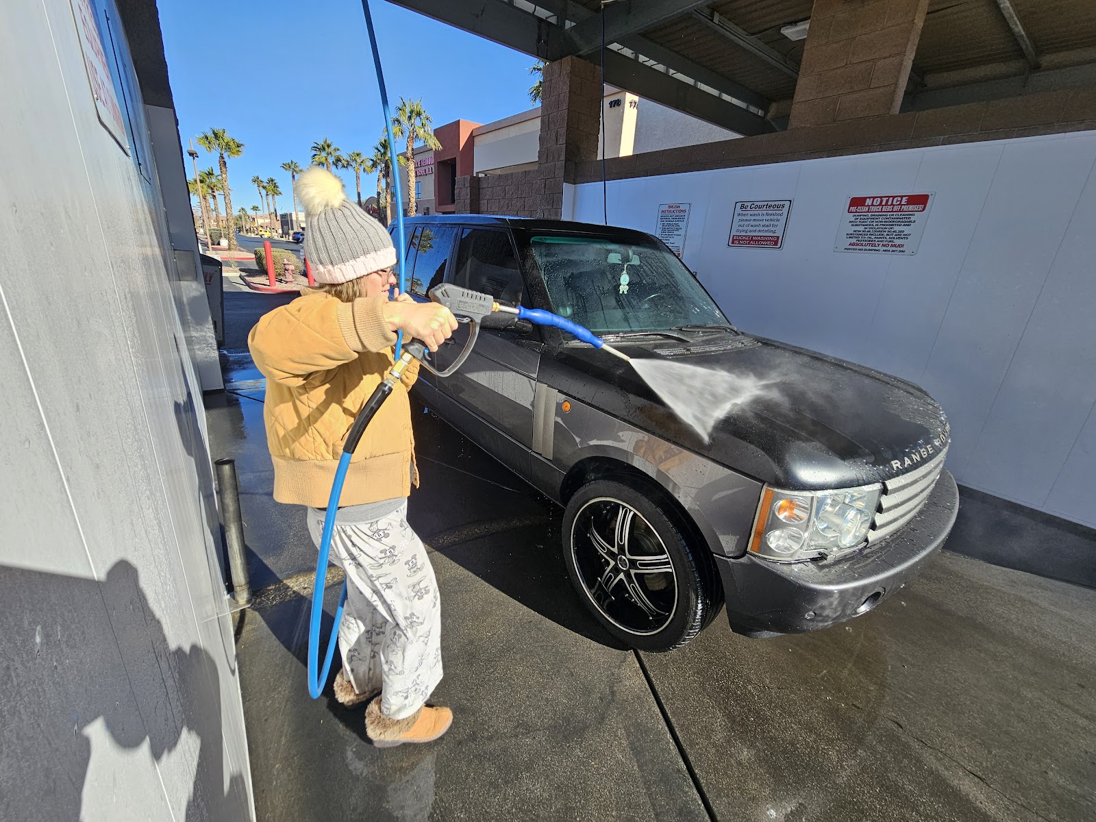Woman pressure washing a Range Rover in a self-serve wash bay