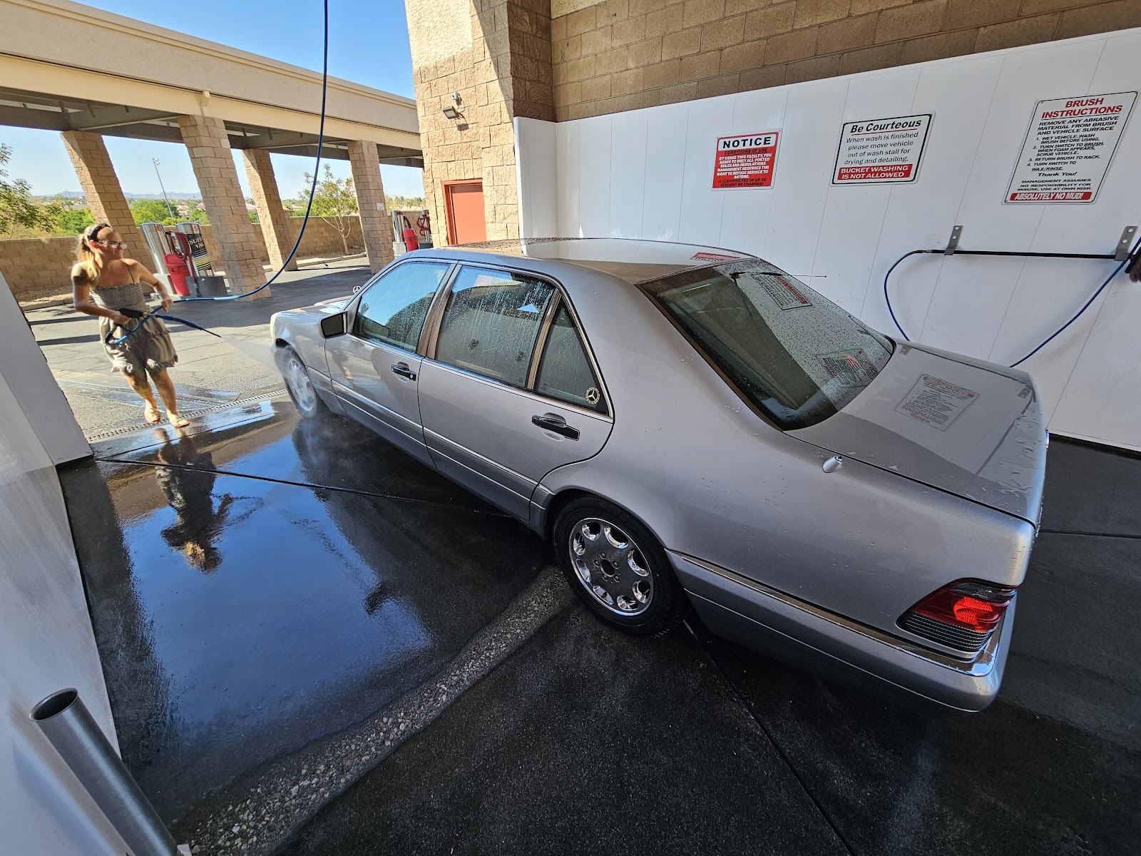 Person washing a silver Mercedes-Benz S-Class sedan at a self-serve wash bay